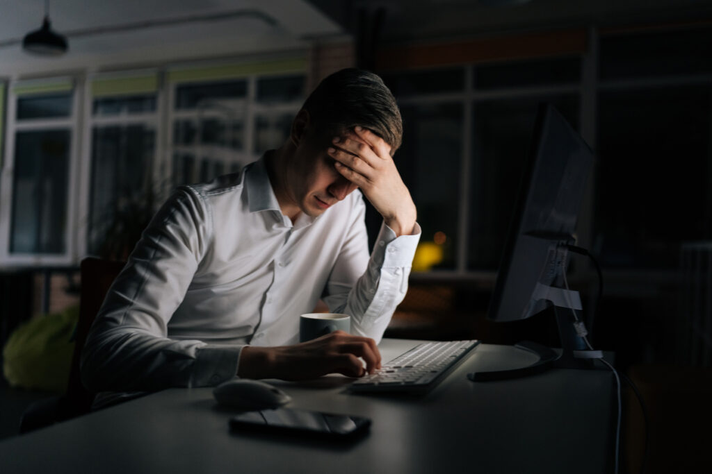 Exhausted businessman working in evening office alone. Tired anxious manager losing failure working on computer at late night. Tired worried business man at workplace